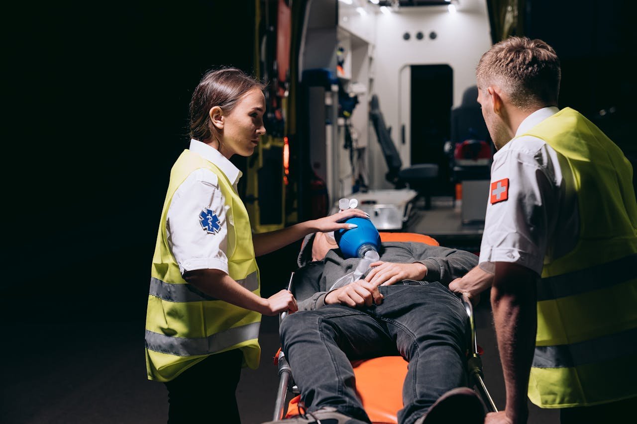 Paramedics in reflective uniforms assist a patient on a stretcher near an ambulance at night.